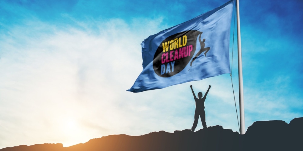 Plakatmotiv zum World Cleanup Day Rechts im Bild eine Flagge mit der Aufschrift World Cleanup Day, darunter die Silhouette eines Menschen, im Hintergrund Sonnenuntergang